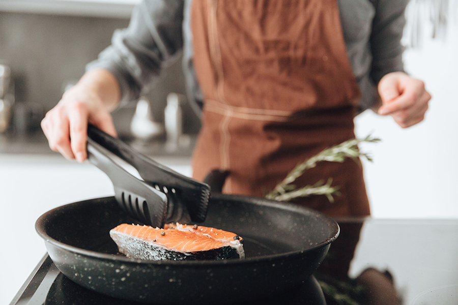 A person wearing an orange apron sautees salmon in a skillet.